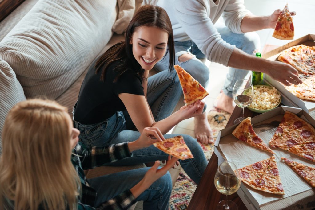 Side view of friends eating pizza in house